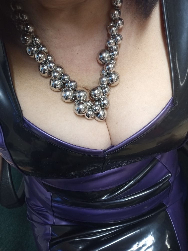 North East pro domme Mistress Orchid in purple latex showing deep cleavage